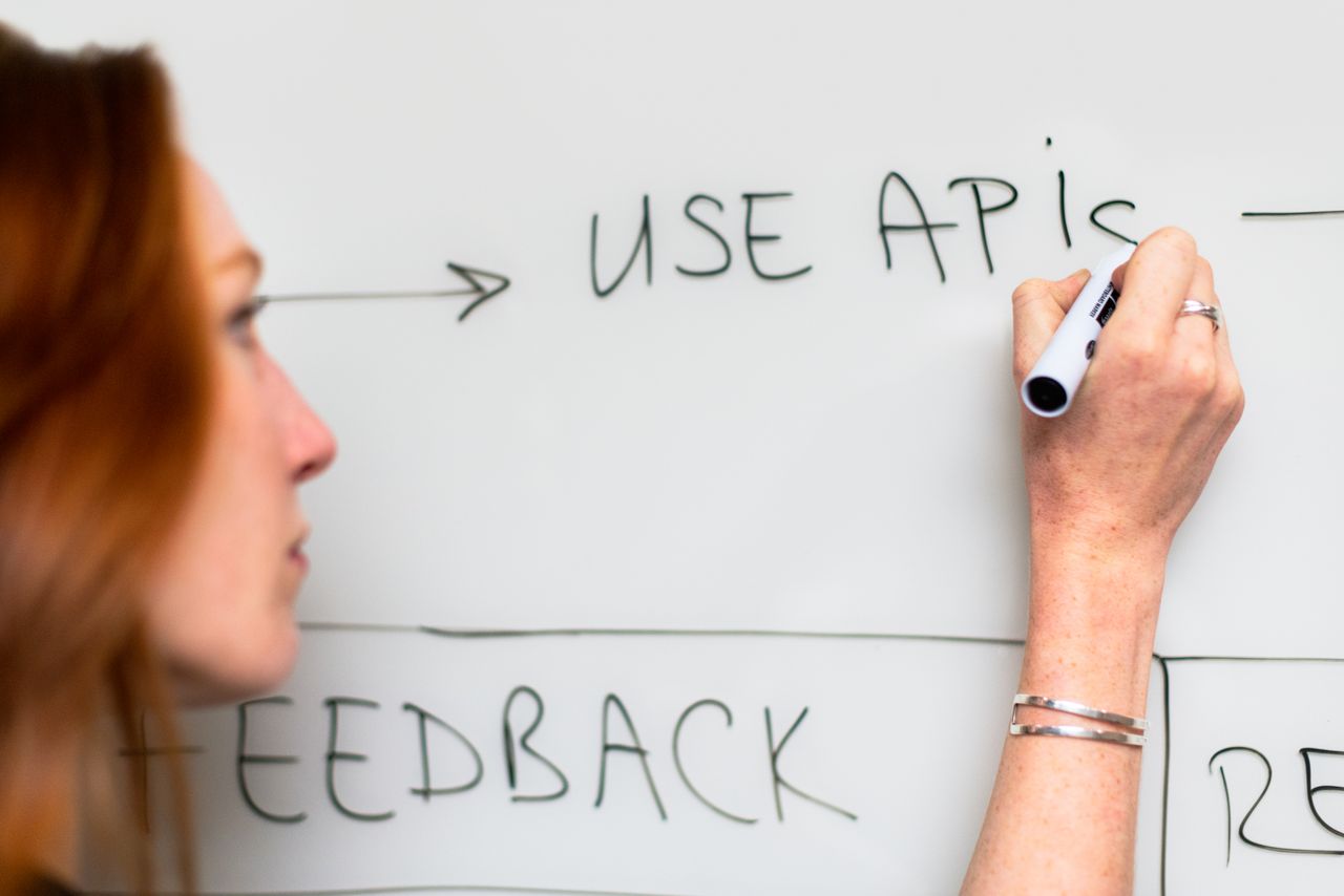 services-04 A woman writes 'Use APIs' on a whiteboard, focusing on software planning and strategy.